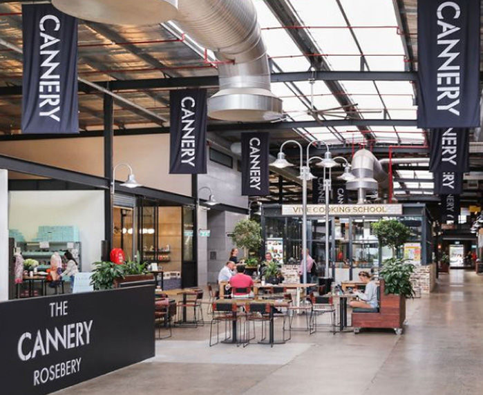 Interior view of The Cannery in Rosebery, showcasing an industrial-style eatery with tables, plants, and banners hanging from the ceiling, creating a vibrant communal space