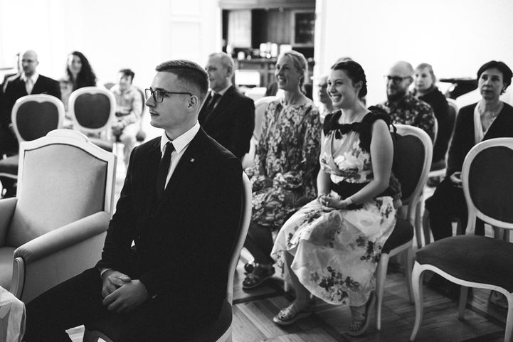 Menschen sitzen auf Stühlen für die Zeremonie, lächeln und schauen aufmerksam zu.