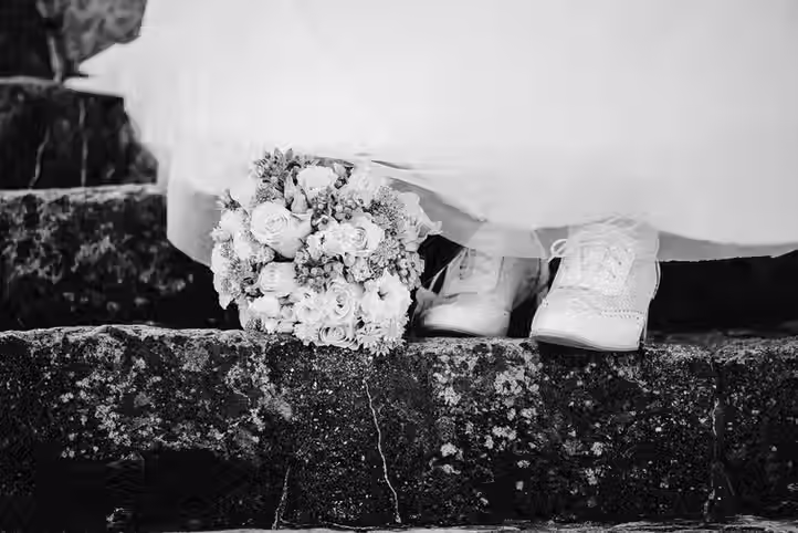 Brautkleidsaum, Brautschuhe und Brautstrauß sind auf einer steinernen Treppe angeordnet.