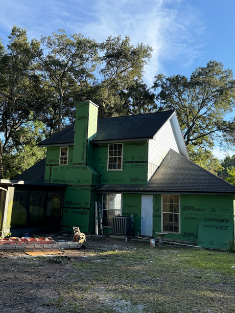 House under construction with green ZIP wrap, windows, and chimney; FLOCON Contractors LLC.