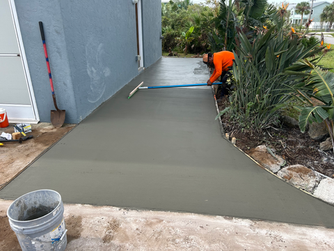 Construction worker smoothing wet concrete on a walkway near a building FLOCON Contractors LLC