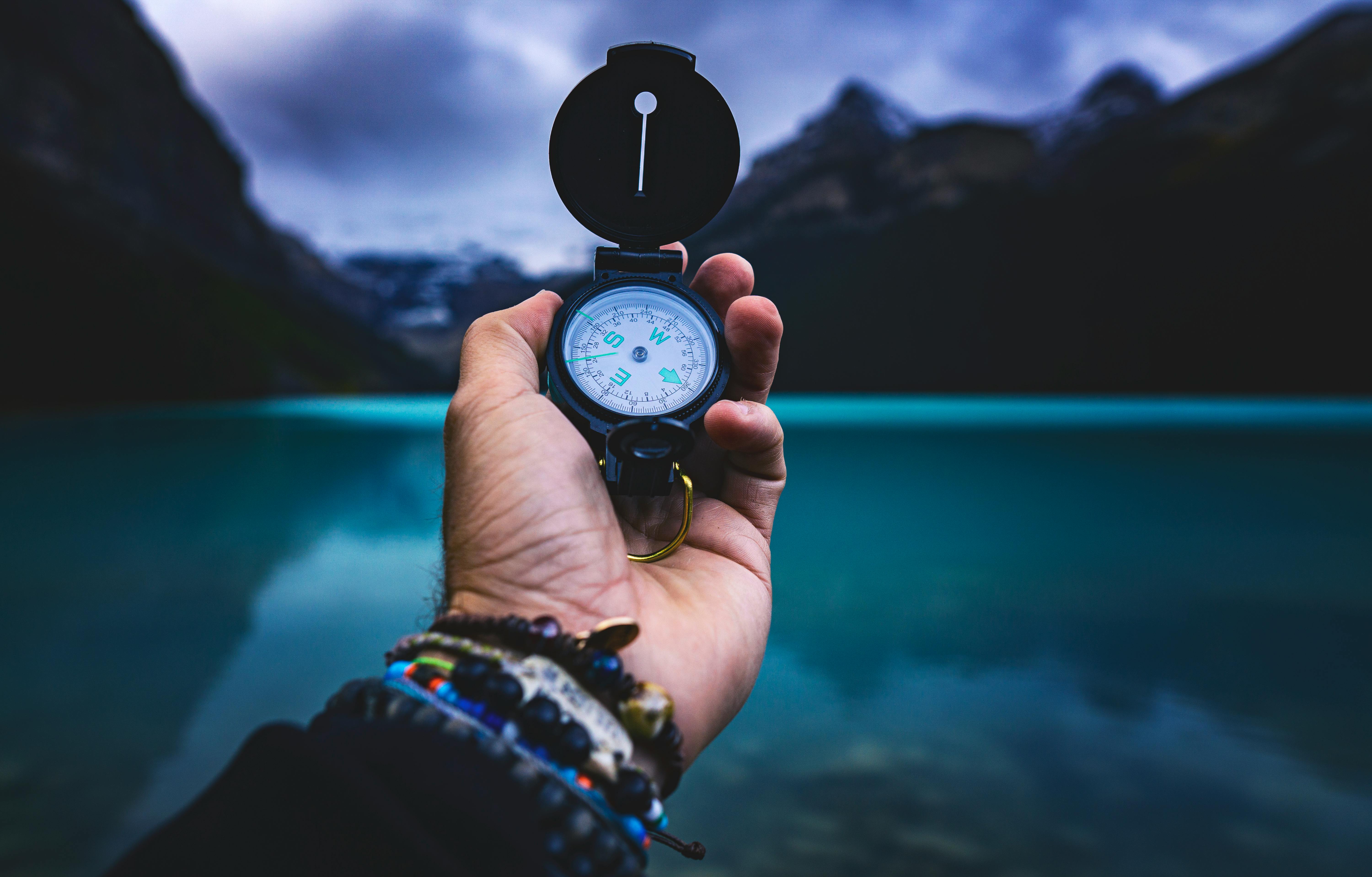 A hand holding a compass against a backdrop of a turquoise lake and mountains, symbolizing purpose as a guiding force in life's journey.