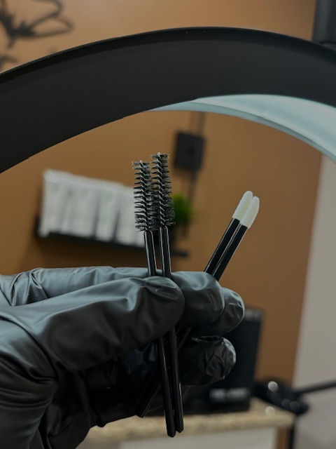 Hand with tools, brow brushes, background with Sincerely Monee Esthetics, LLC