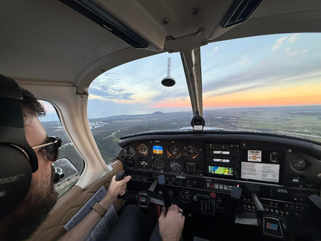 A pilot wearing glasses flies a Piper PA-28 over the Australian coast.