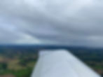 Aircraft wing over patchwork farmland under cloudy skies, creating a serene aerial view with muted greens and browns.