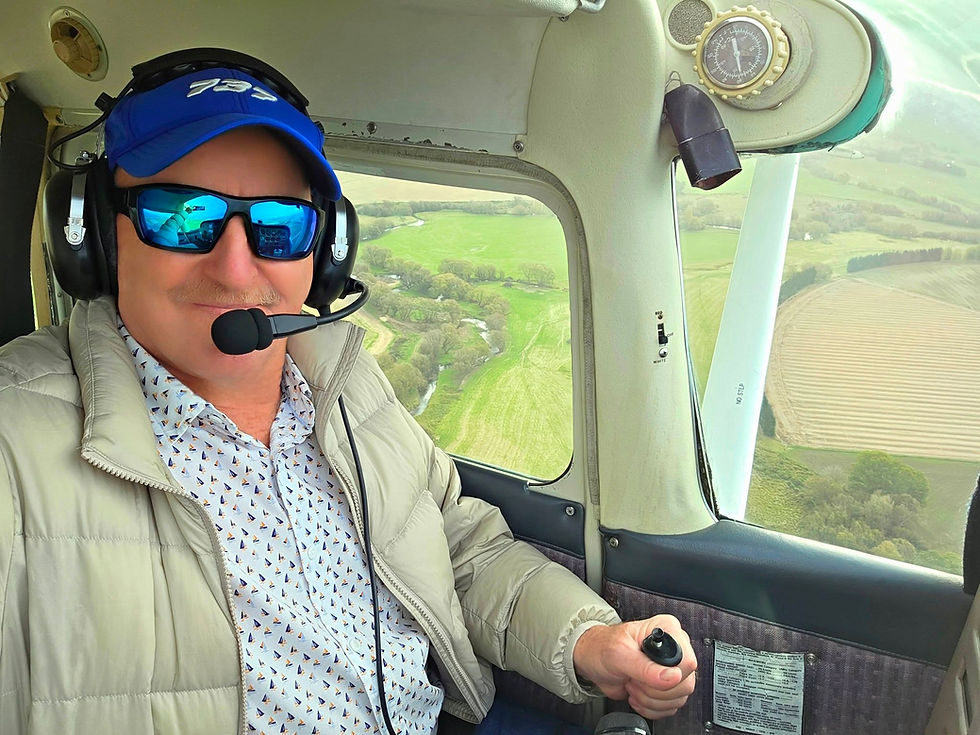 A pilot wearing a headset at the controls of a Cessna, with countryside visible through the window.