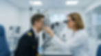 Optometrist examines pilot using eye test machine in a clinical setting. Eye chart in background, both focused.