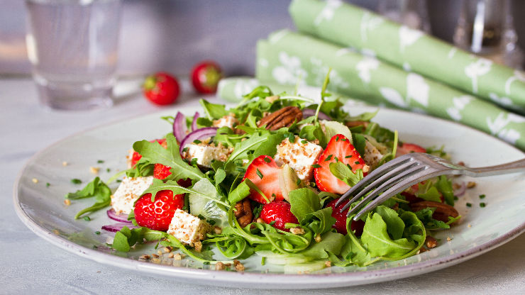 Salata od rikole, ljubičastog luka, feta sira i jagoda na bijelom tanjuru s vilicom