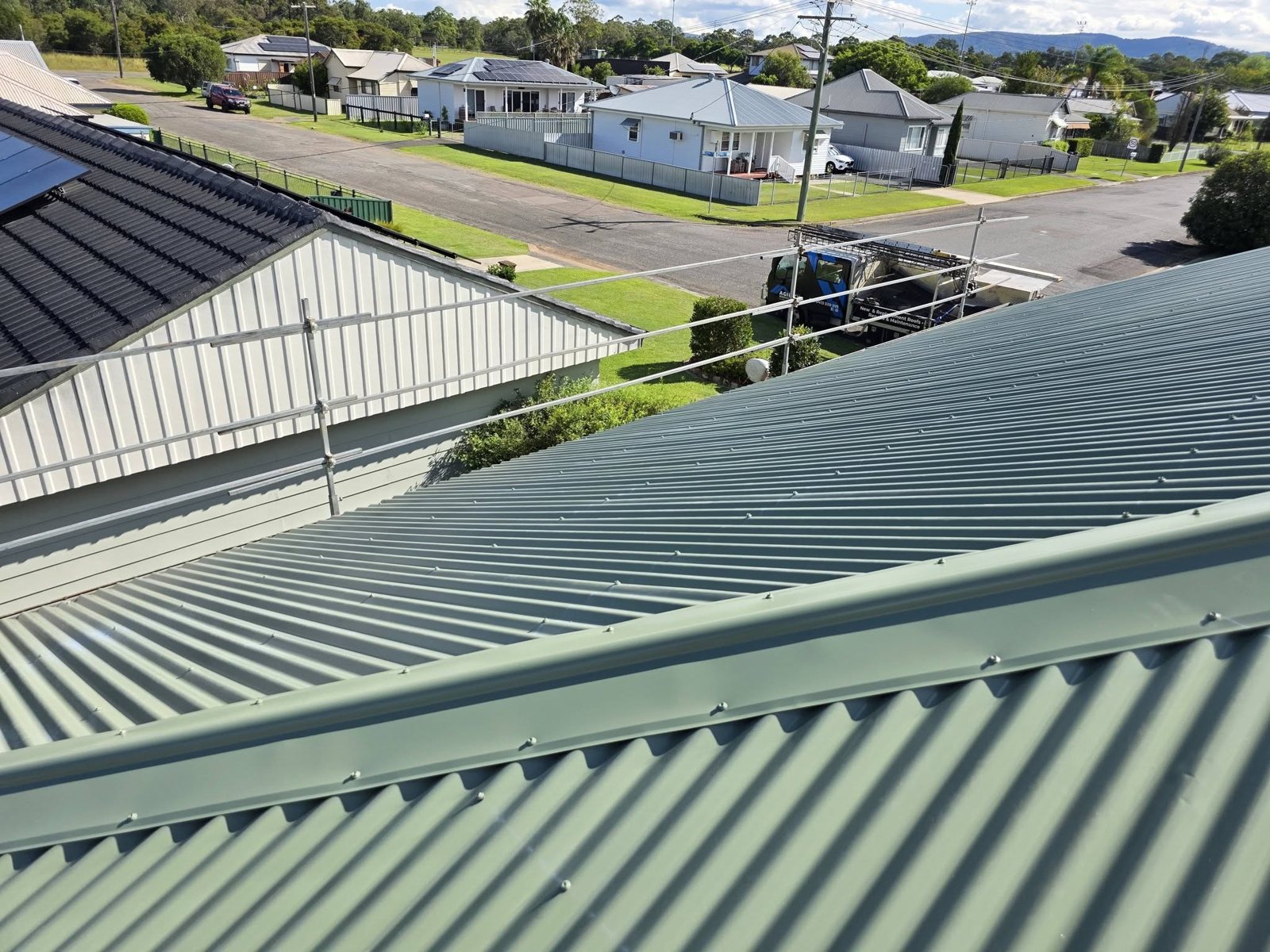 New green corrugated metal roof after a tile to metal re-roof, with scaffold and the Agility Roofing truck below