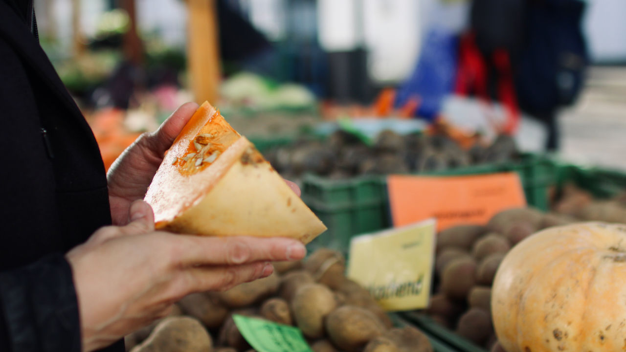 Hand mit Kürbis in Hand vor Marktstand auf dem Arlesheimer Gemüsemarkt