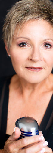 White woman 50+ holding microphone, gazes softly at camera