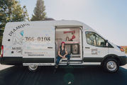 Liz sitting on the edge of the van with her standard poodle in his kennel