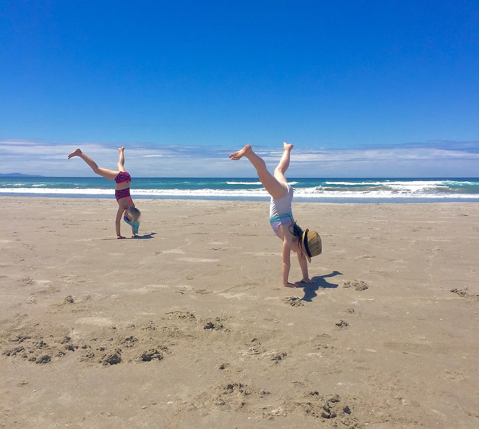 two kids doing cartwheels in sand on beach with ocean in background