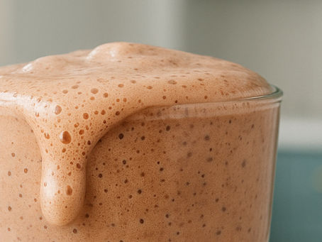 An overflowing chocolate protein shake in a glass
