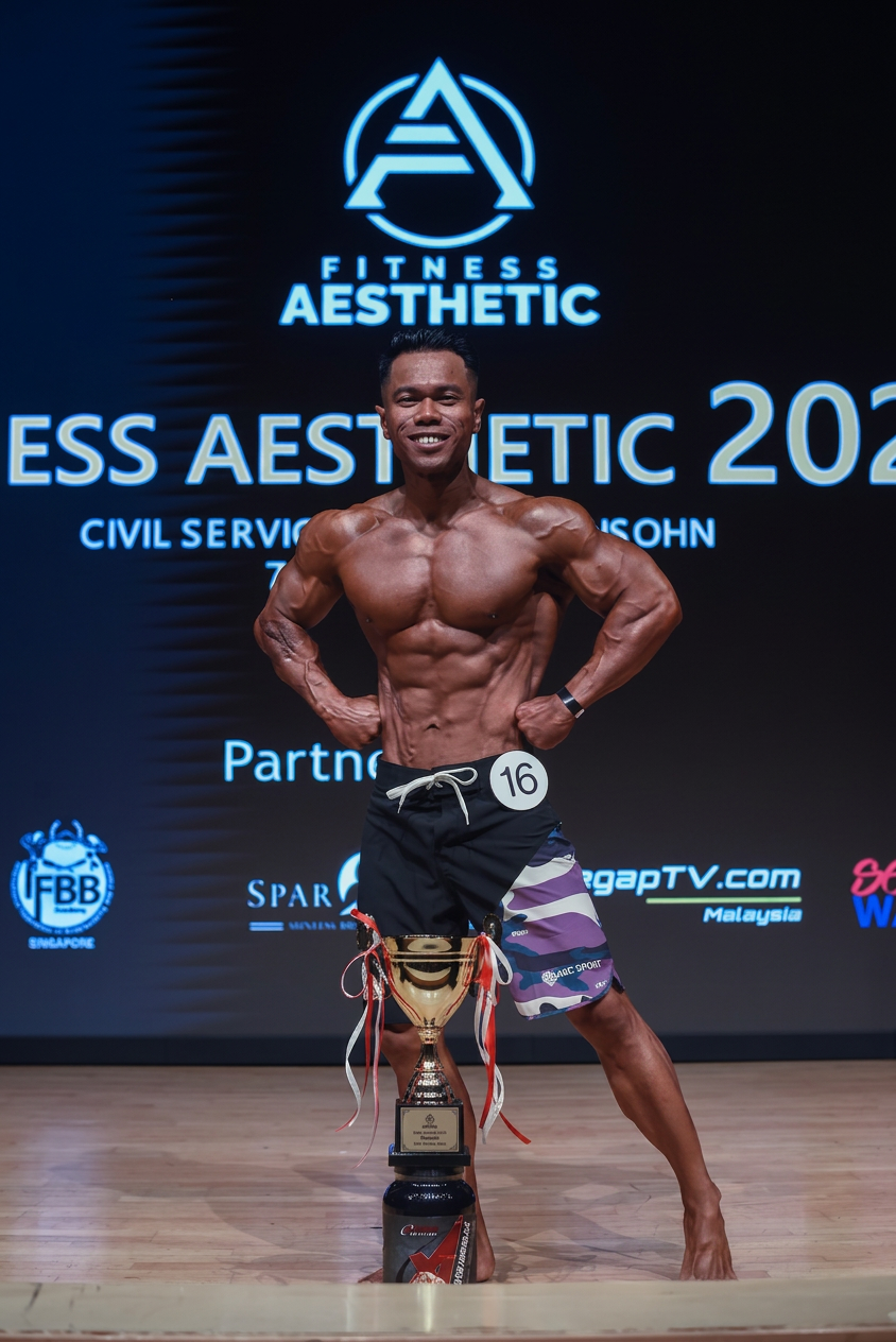 Past male physique competitor posing with trophy