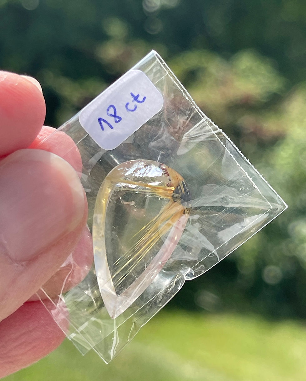 fingers holding golden rutile half star quartz cabochon in cellophane