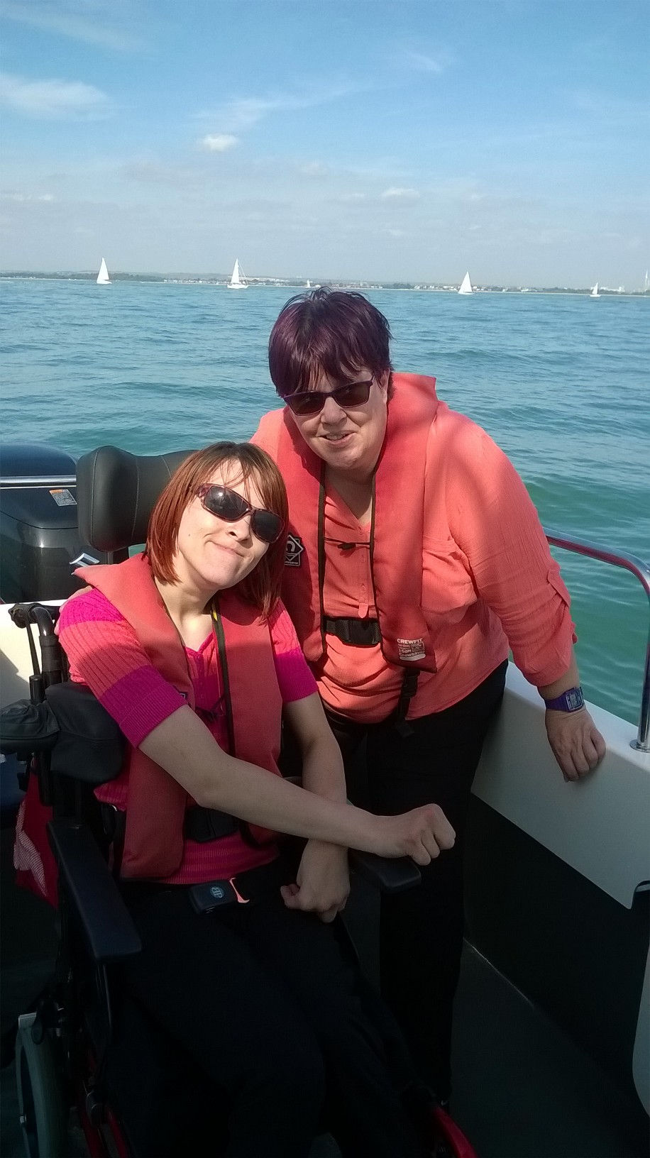 Ailsa and her mum on a speed boat. Both have sunglasses on. Blue sky.