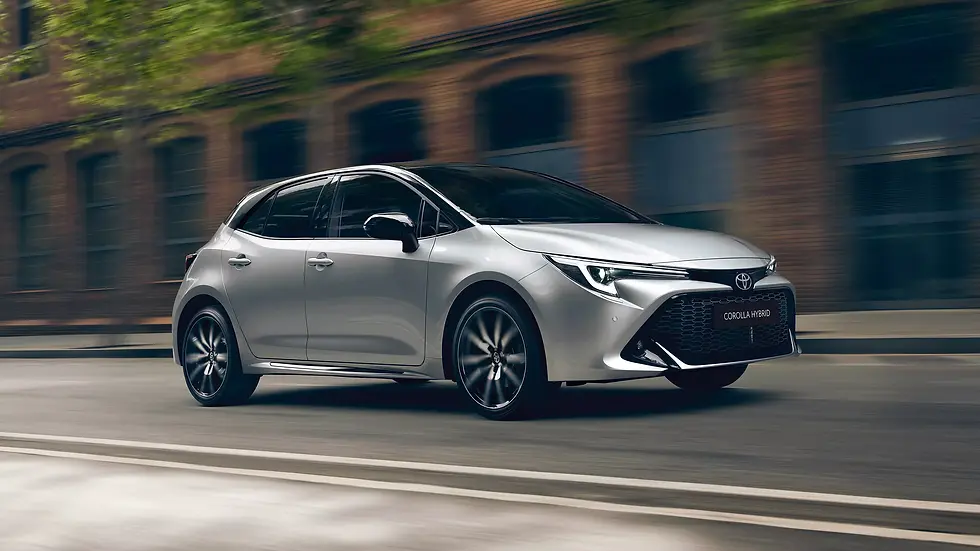 Silver Toyota Corolla Hybrid drives down a city street, blurred brick buildings in background, sleek design and dynamic motion.