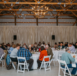 A large group of individual sits at round white tables in the reception hall