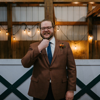 The groom stares into the camera in a brown suit with his hand on his chin