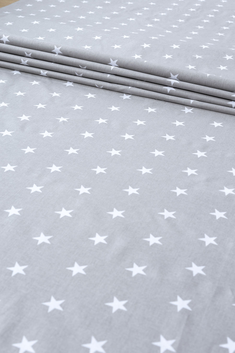 Tkanina bawełniana w białe gwiazdki na szarym tle, prezentowana w złożonej formie. Wysokiej jakości materiał o gramaturze 130