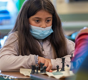 A girl wearing a covid mask thinking about her next chess move