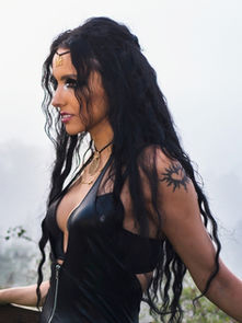 Woman with long black hair and tattoo in black outfit stands on a foggy balcony, looking elegant and peaceful amidst a misty forest.