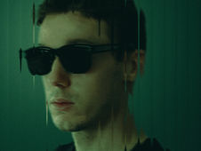Man wearing sunglasses, reflected in distorted glass, green background. Mysterious and moody atmosphere.