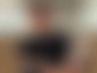 Man in black outfit and sunglasses sits on stairs, urban background. Tattoo and "AKOR" shirt visible, conveys a relaxed, cool vibe.