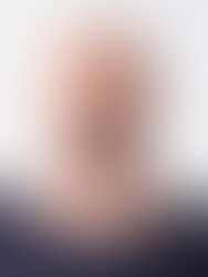 Bald man with a beard in a black shirt, standing against a plain white background, looking directly at the camera with a neutral expression.