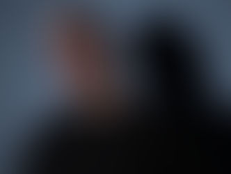 Man in sunglasses and black shirt against a gray backdrop, casting a distinct shadow. Moody and contemplative expression.