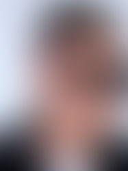 Man with short hair in sunglasses and a black leather jacket looks to the side against a plain white background.