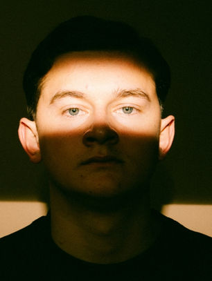 A man's face is partially illuminated by a horizontal beam of light, creating a dramatic contrast. The background is dark, evoking a moody atmosphere.