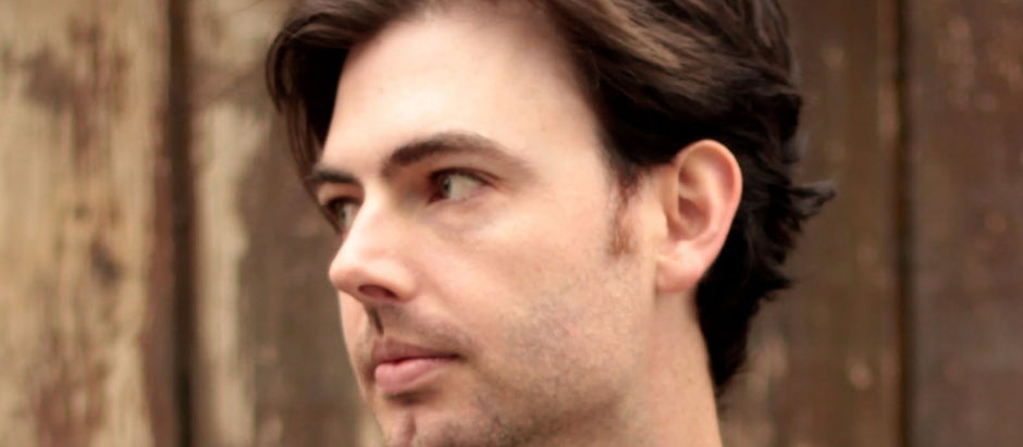 Close-up of a thoughtful young man looking left against a blurred wooden background.