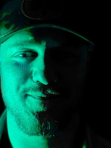 Man in a cap partially lit by green light, standing against a dark background, exudes a mysterious mood.