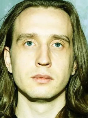 Man with long brown hair stares at camera. Background features a green, blurred forest scene, creating a calm and introspective mood.