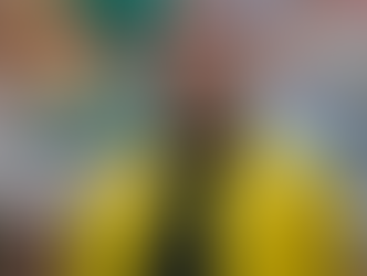 Man in a bright yellow jacket stands in front of a mural with colorful artwork. He has a calm expression. Urban setting.