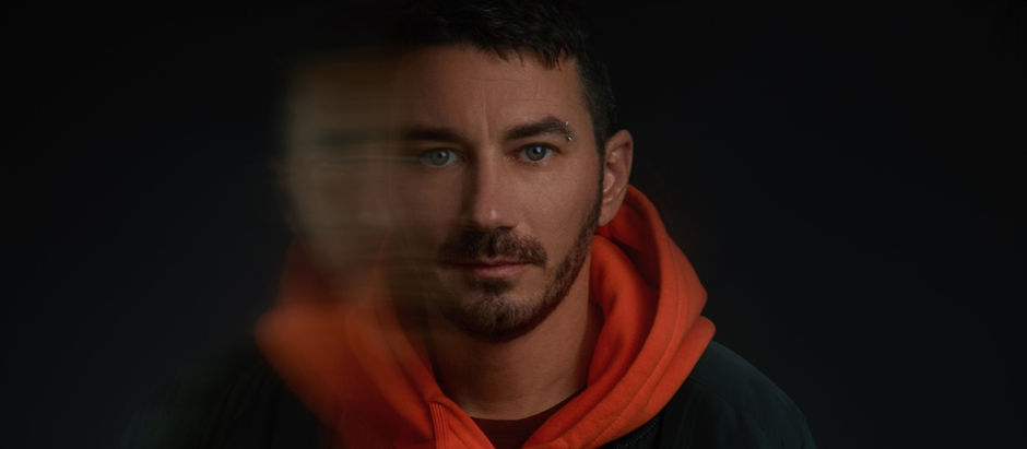 Man in orange hoodie against dark background, face partially blurred, conveying a mysterious mood.
