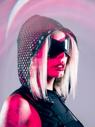 Futuristic portrait of a woman in a mesh hood and black visor, lit pink against a gray background.