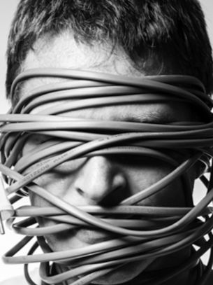 Black-and-white portrait of a man with an electrical cord wrapped around his face, plug hanging beside him, looking tense.