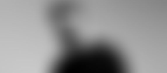 Bearded man in black shirt with neutral expression against a plain gray background. Monochrome style, conveying a calm mood.