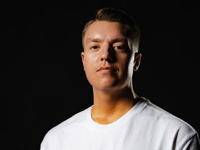 Portrait of a young man in a white shirt against a black background, looking serious and calm.