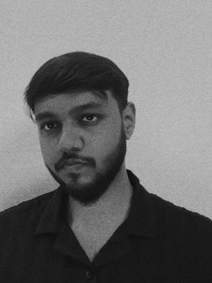 Black-and-white portrait of a young man with a beard against a plain wall, looking serious and contemplative.