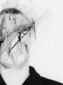 Distorted black-and-white image of a person with a cracked, abstract face. The background is plain white, creating an eerie atmosphere.