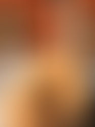 Two people wearing sunglasses smile and relax on a patio with red fence background. One wears a patterned black shirt, the other a striped jacket.