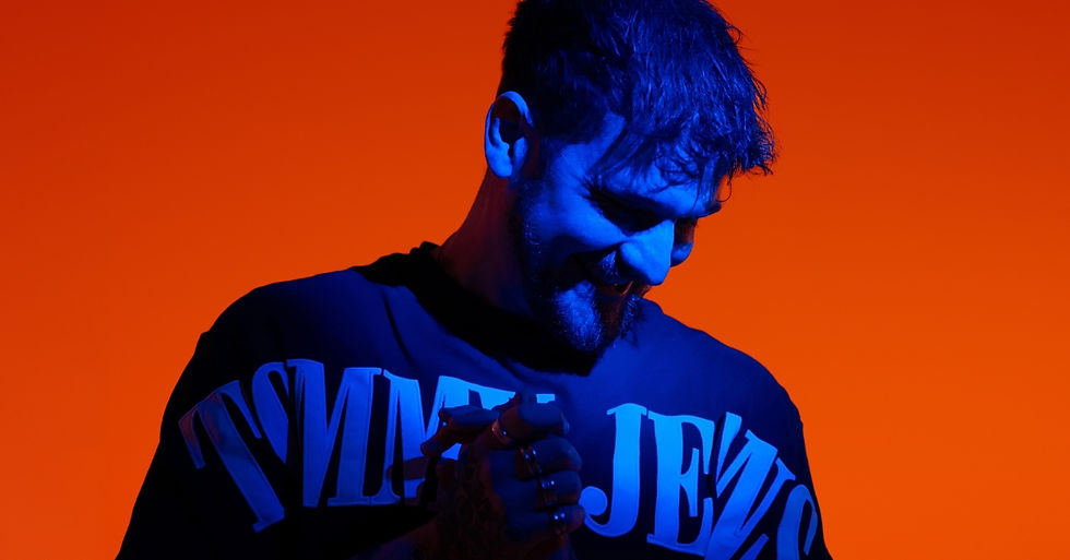 Man in a blue-lit shirt with bold text, smiling against a vibrant orange background, creating a contrasty and energetic mood.