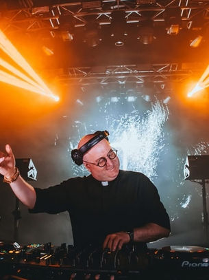 DJ performing energetically with headphones in a vibrant club, surrounded by orange lighting and effects. Mood is lively and engaging.