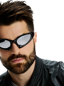 A person with a beard wears sleek black sunglasses and a leather jacket, set against a plain white background, exuding a cool, modern vibe.