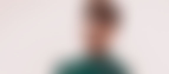 Young man with brown hair and a green shirt looks into the camera against a plain white background, conveying a calm mood.