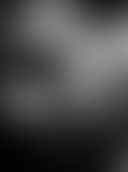 Black and white portrait of a man looking down, wearing a chain necklace. The mood is contemplative, with a dark background.